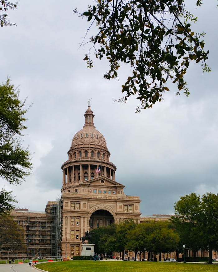 Historic Texas State Capitol building framed by trees under a cloudy sky in Austin.